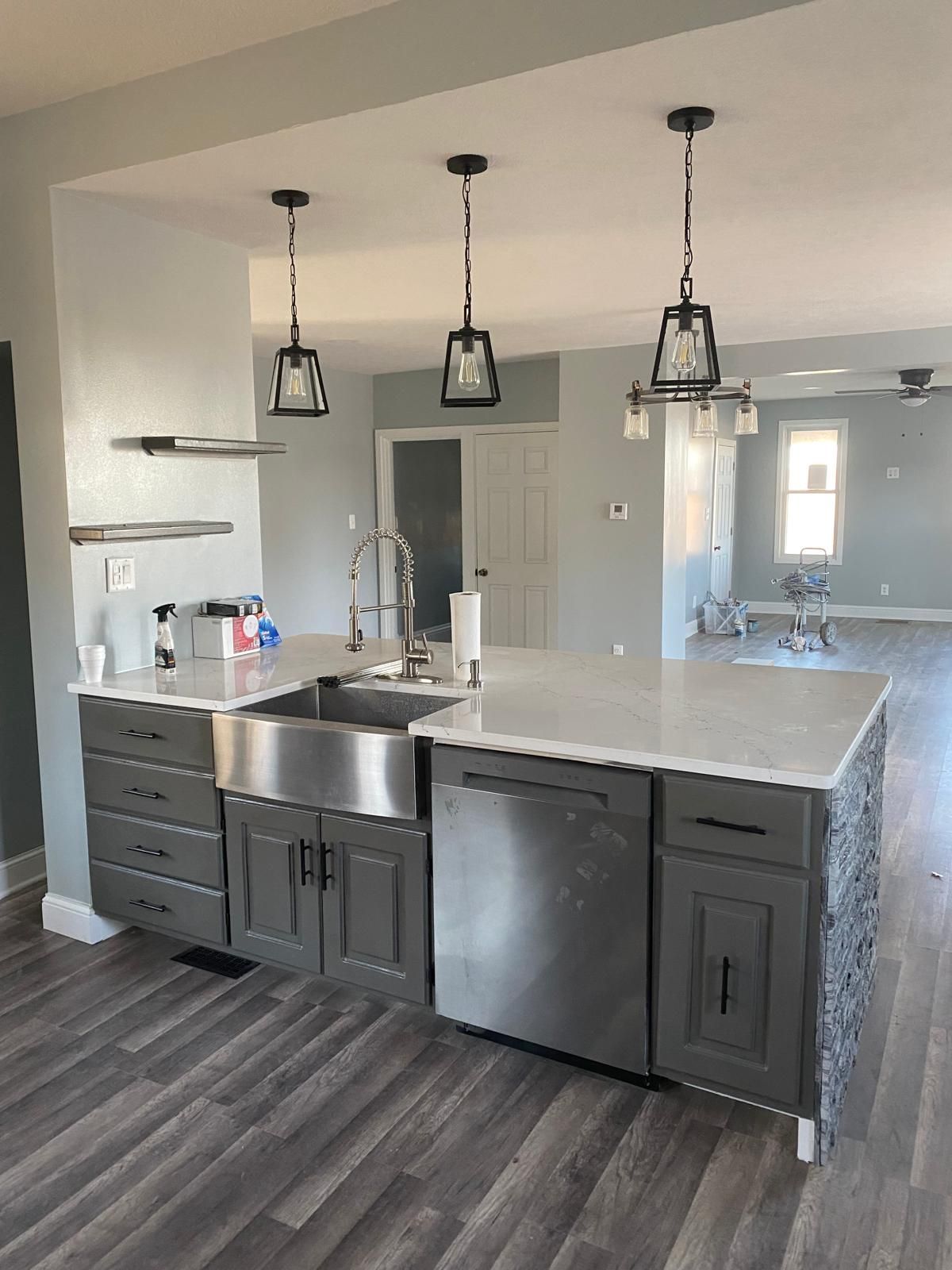 A kitchen with gray cabinets , a stainless steel sink , a dishwasher , and a large island.