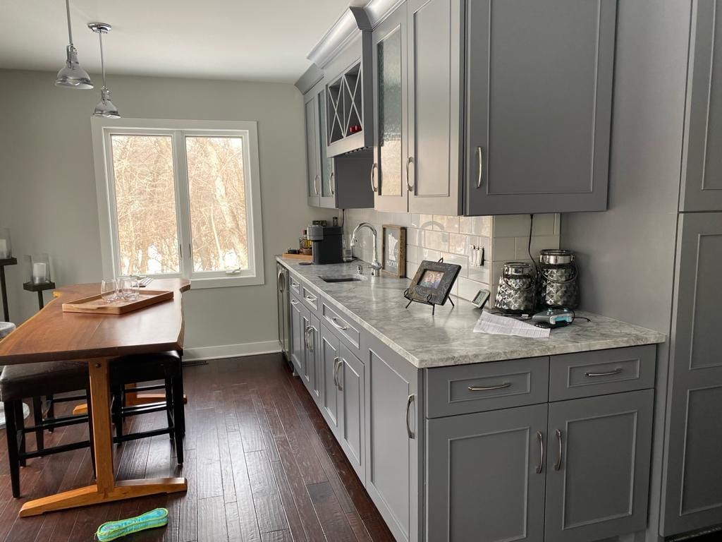 A kitchen with gray cabinets , granite counter tops , a table and chairs.