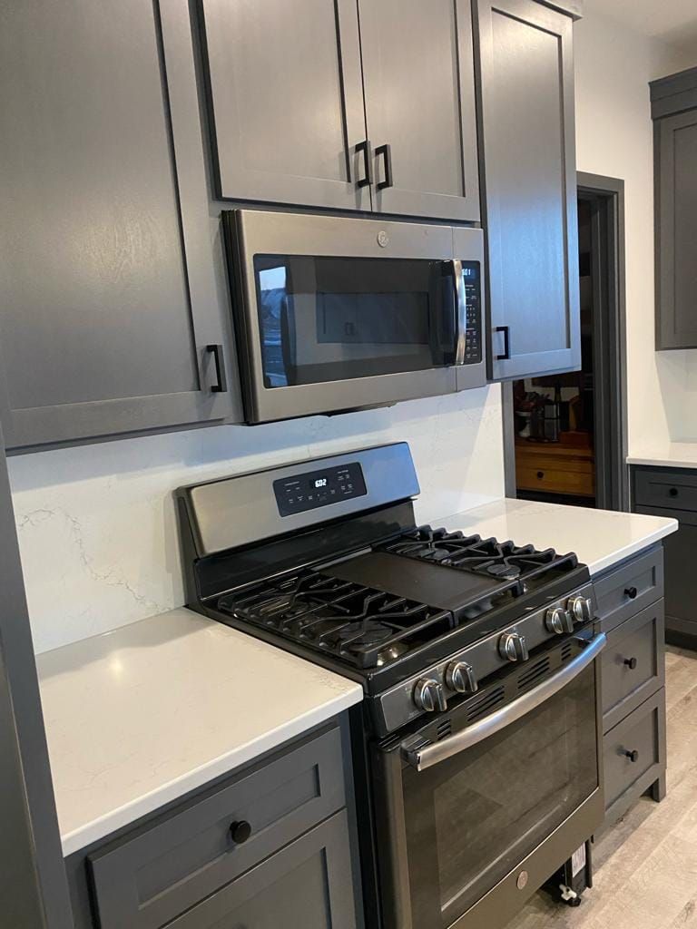 A kitchen with a stove , microwave , and gray cabinets.