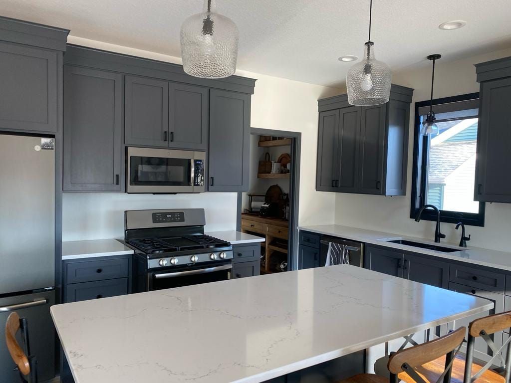 A kitchen with gray cabinets , white counter tops , a stove , microwave and a large island.