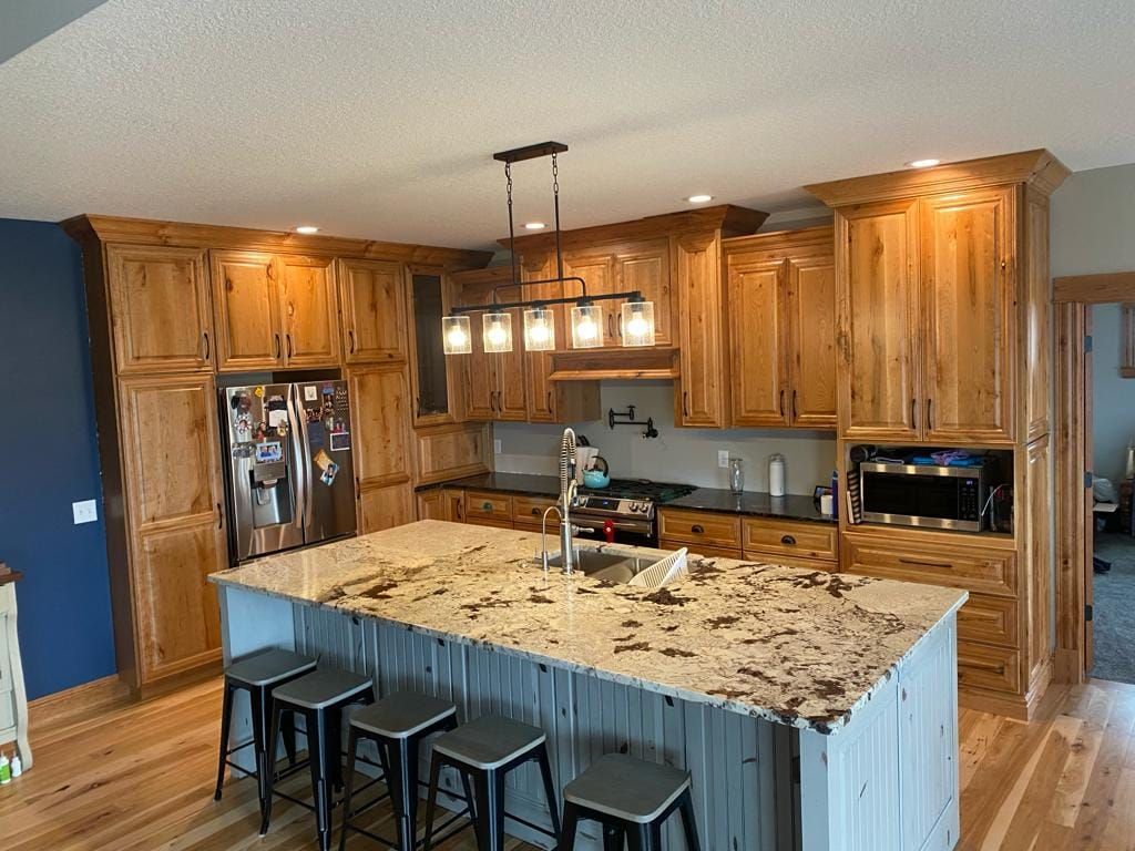 A kitchen with wooden cabinets , granite counter tops , stools and a large island.