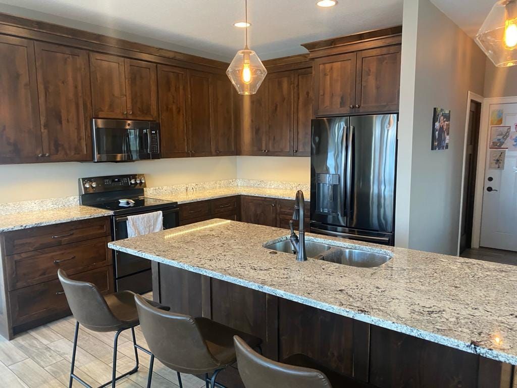 A kitchen with granite counter tops , stainless steel appliances , wooden cabinets and a large island.