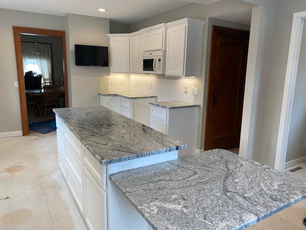 A kitchen with granite counter tops , white cabinets , and a large island.
