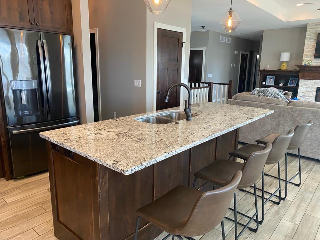 A kitchen with a large island , stools , a refrigerator and a sink.