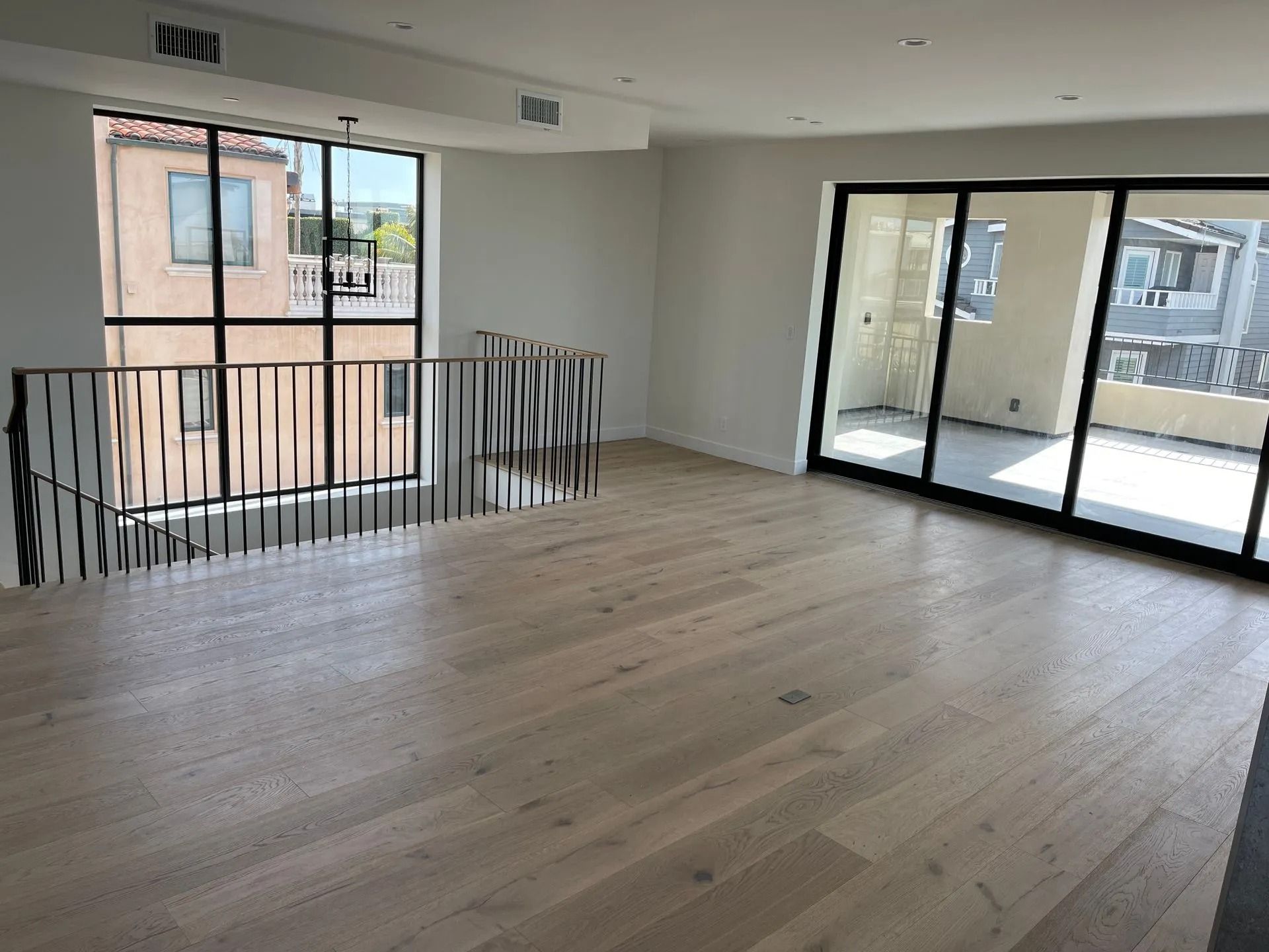 Empty room with light wood floors, large windows, and a black railing.