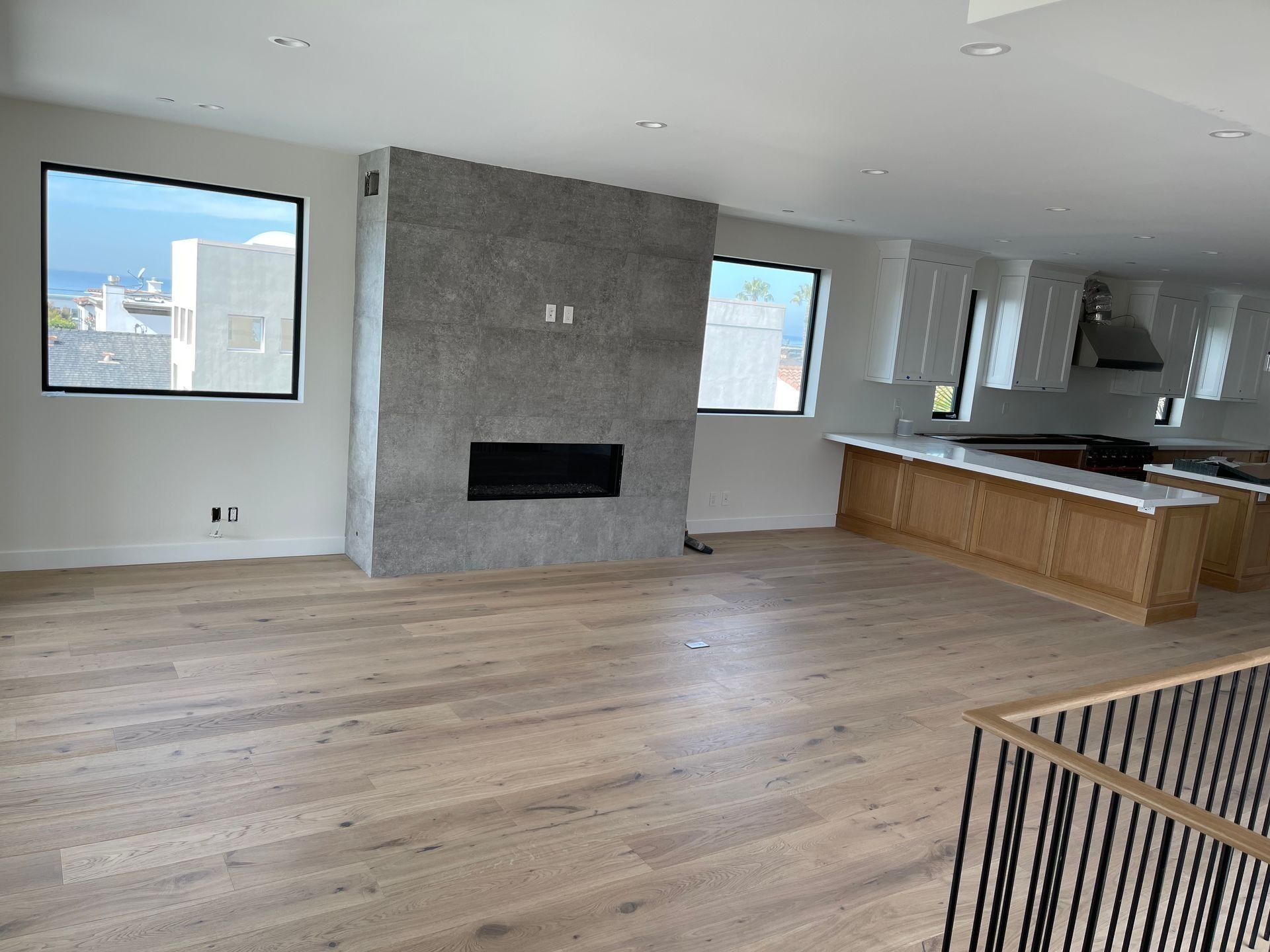 Spacious living room with fireplace, kitchen, and light wood floors. Large windows with a cityscape view.