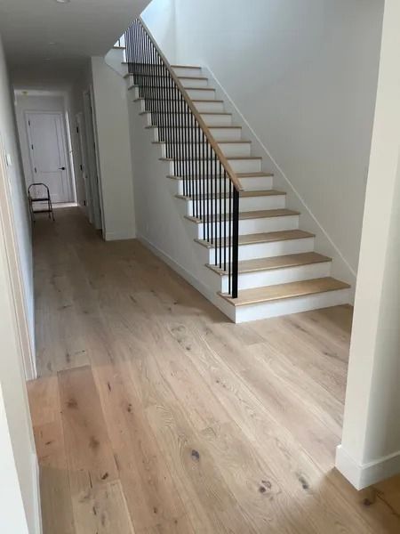 Hallway with wood floors, stairs with black railings, and white walls.
