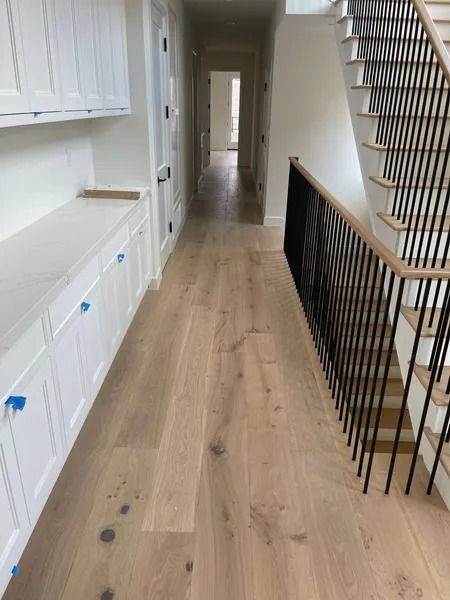 Hallway with wood floors, built-in white cabinets, black stair railing, and a staircase.