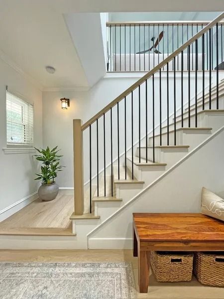 Staircase with light wood steps, black metal balusters, and a wooden bench with storage baskets.