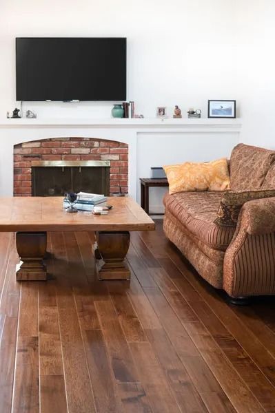 Living room with a fireplace, TV, brown couch, wooden coffee table, and hardwood floors.