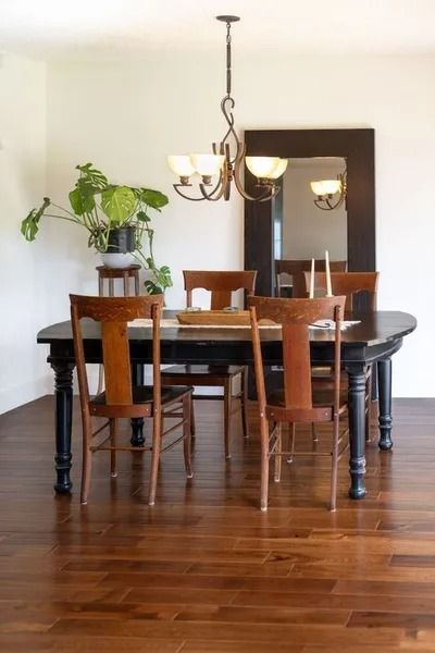 Dining room with dark table, wooden chairs, large mirror, and plant.