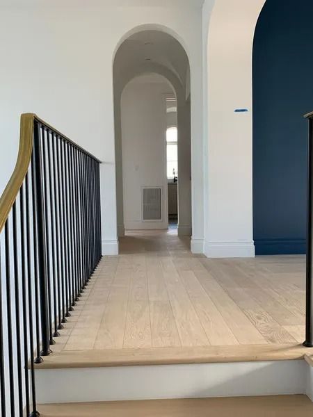 Hallway with light wood floors, white walls, and arched doorways, leading to a window at the end.