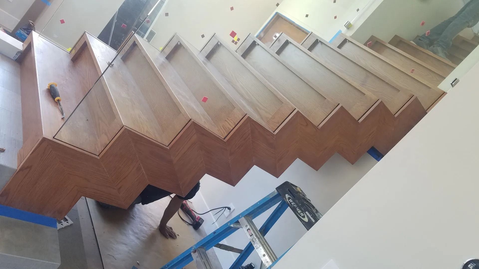 Wooden staircase under construction, brown steps, person working on a ladder.