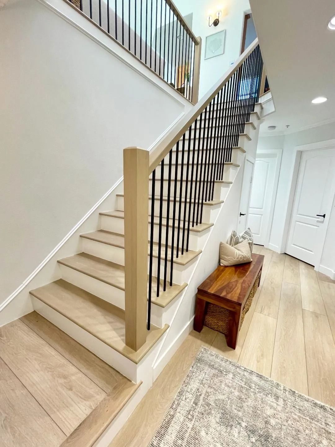 Staircase with wooden steps, black railing, light walls, and a wooden bench.