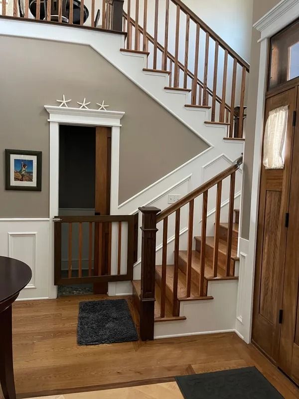 Wooden staircase and doorway with a safety gate in a foyer. Light wood floor and brown walls.
