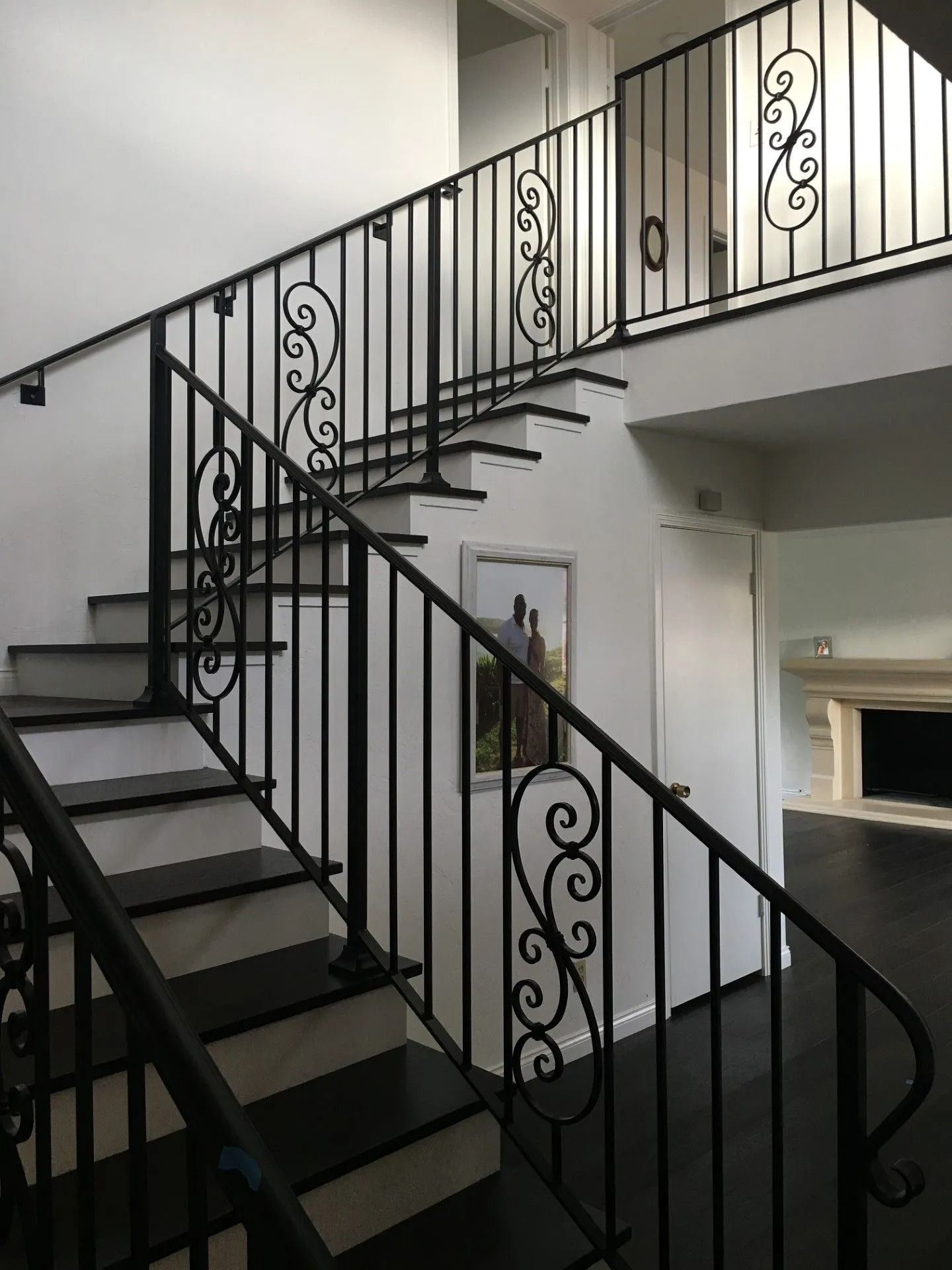 Black iron staircase with decorative scrollwork, leading to a second floor with a white wall and doorway.