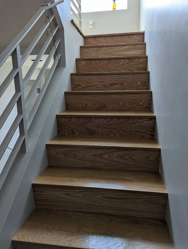 Wooden staircase with silver handrail against a gray wall.