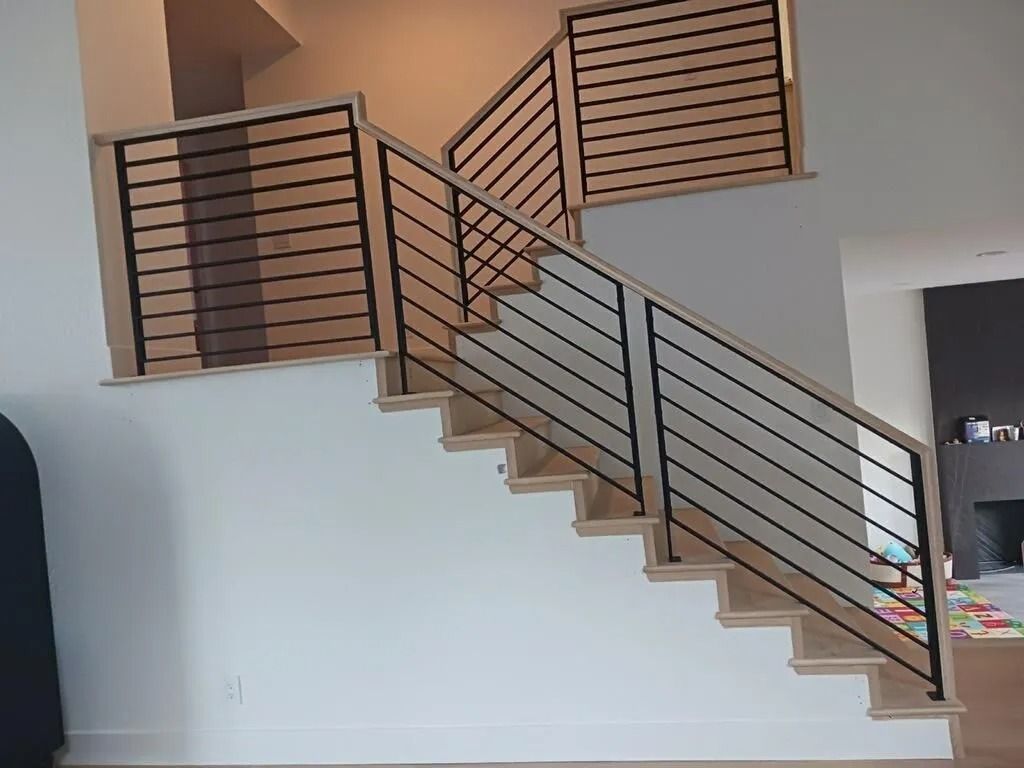 Staircase with wooden steps and black metal horizontal railings. Light walls.