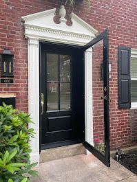 A black front door is open on a brick house.