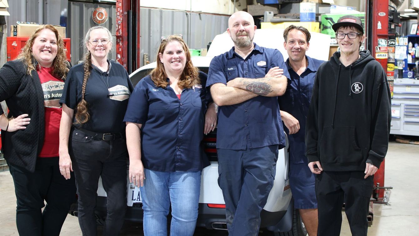 A group of six auto mechanics posing in a garage, smiling.