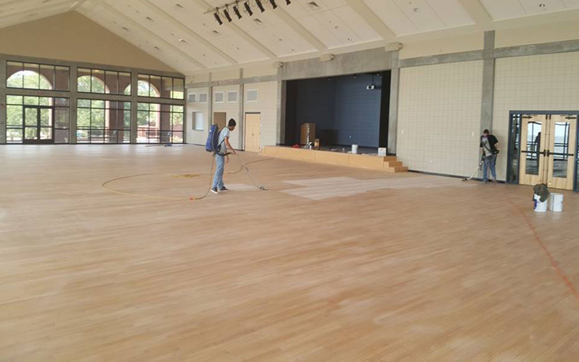A man is cleaning a wooden floor in a large room