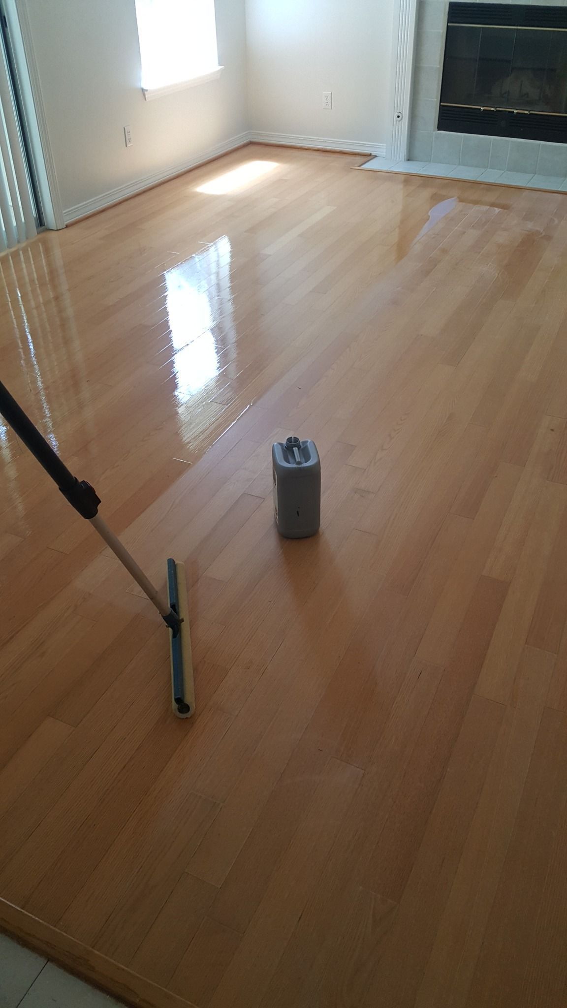 A person is painting a wooden floor in a living room.