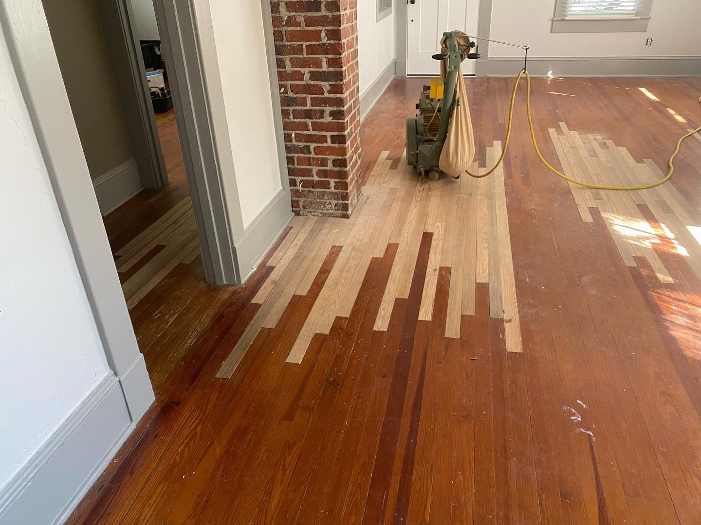 A wooden floor is being sanded with a machine in a room.