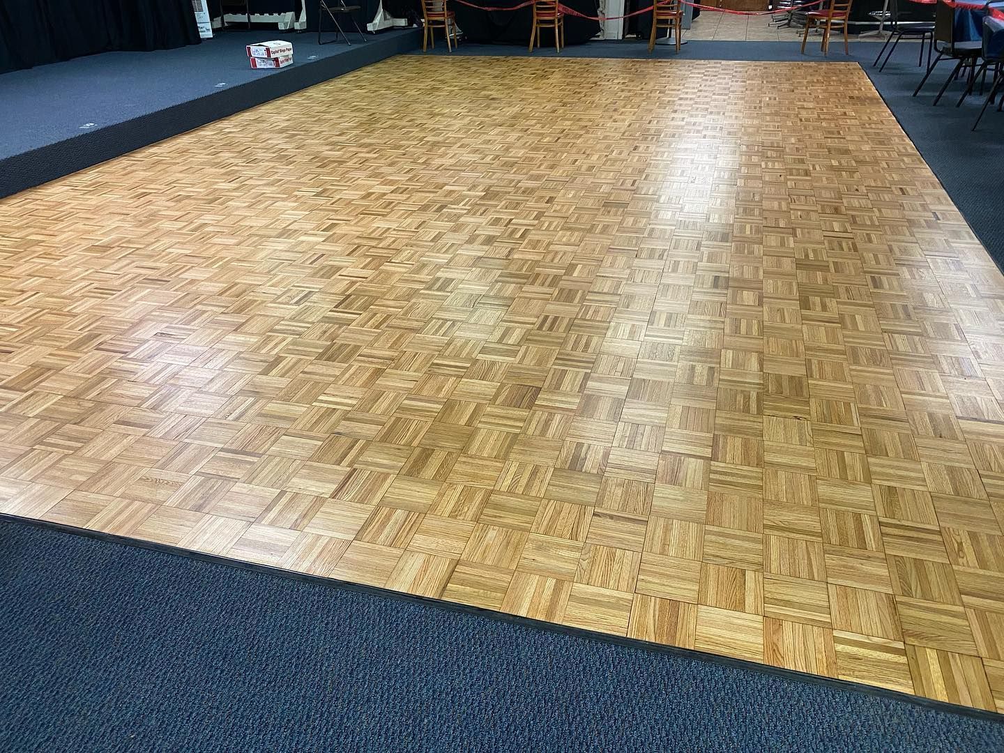 A large wooden dance floor in a room with tables and chairs.