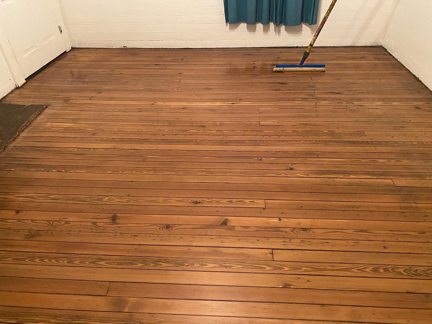 A wooden floor with a broom on it in a room.