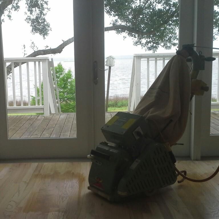 A sander is sitting on a wooden floor in front of a window.
