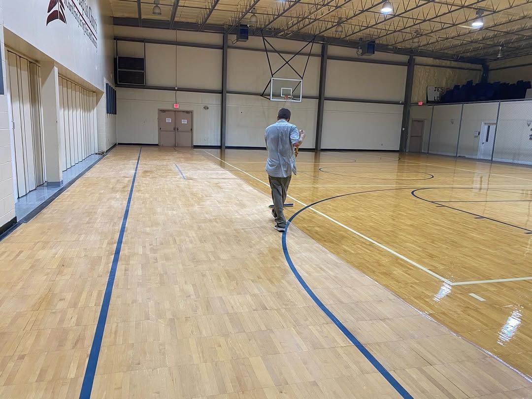 A man is standing on a wooden basketball court in a gym.