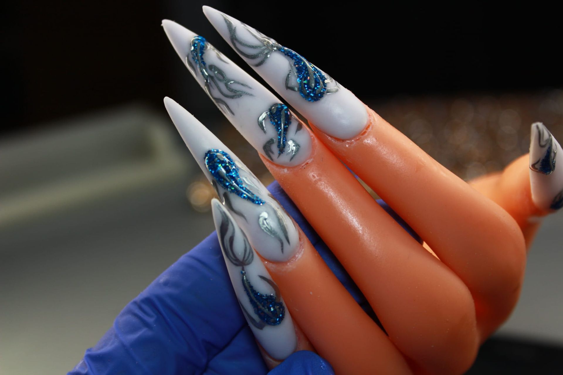 A person wearing a blue glove is holding a fake hand with long nails