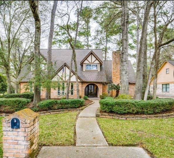A two-story house with a brick mailbox in front, walkway to the arched entrance. Trees surround the house.