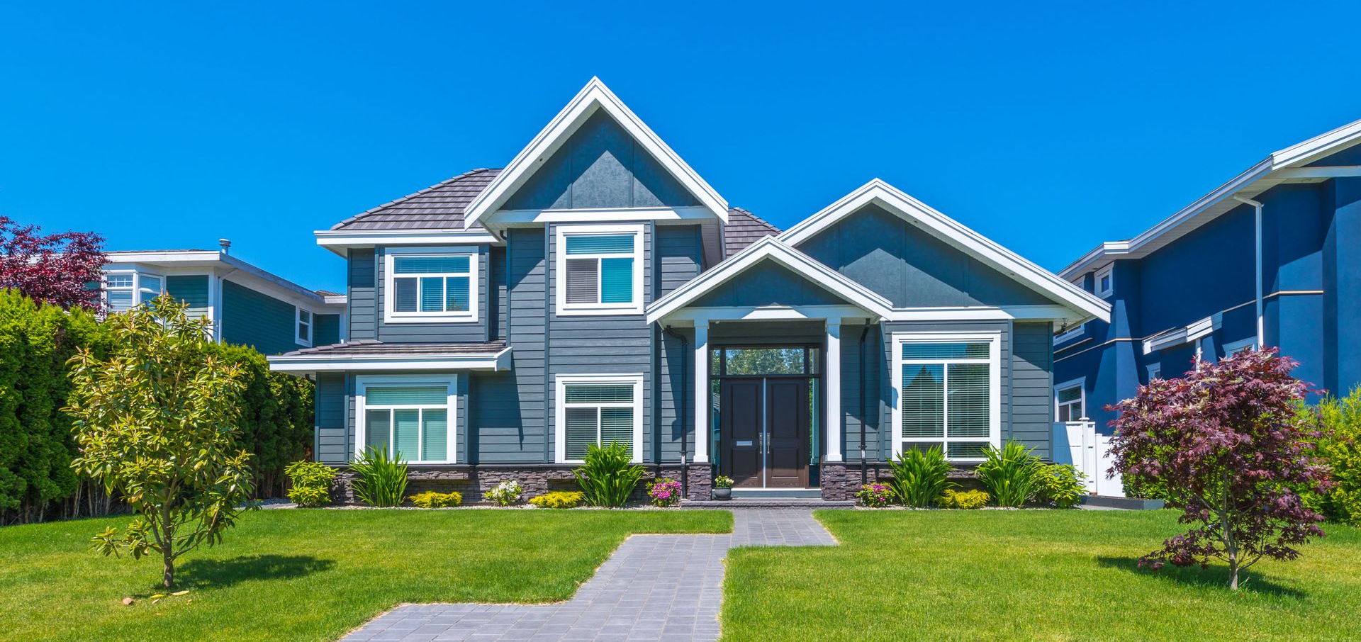 Blue house with white trim, green lawn, and blue sky.