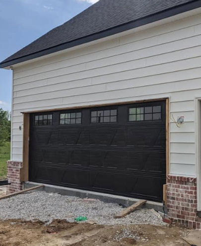 Black garage door on a beige house with brick trim, viewed from a gravel driveway.