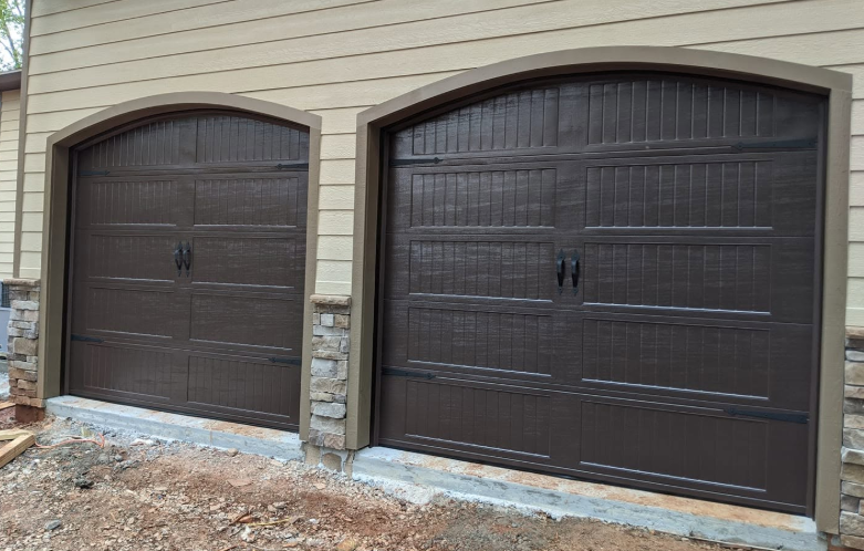 Two dark brown arched garage doors with stone trim on a beige house exterior.