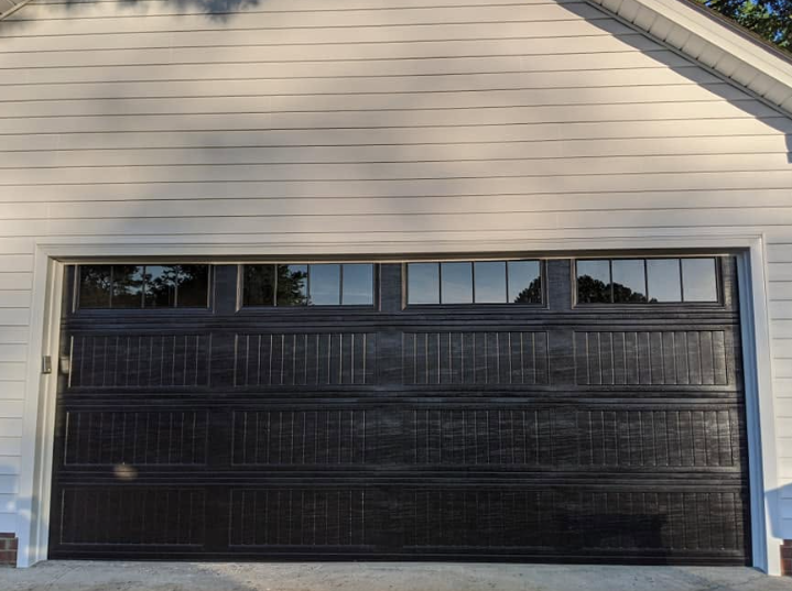 Black garage door on a beige house exterior with small windows along the top.
