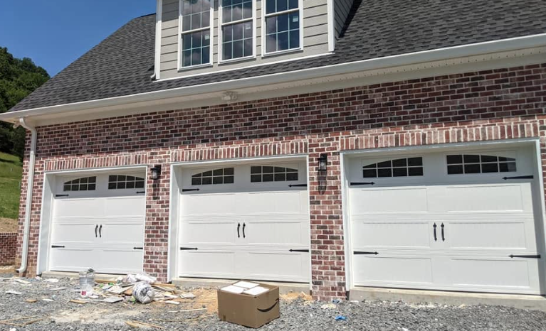 Three white garage doors on a brick house with construction debris in front