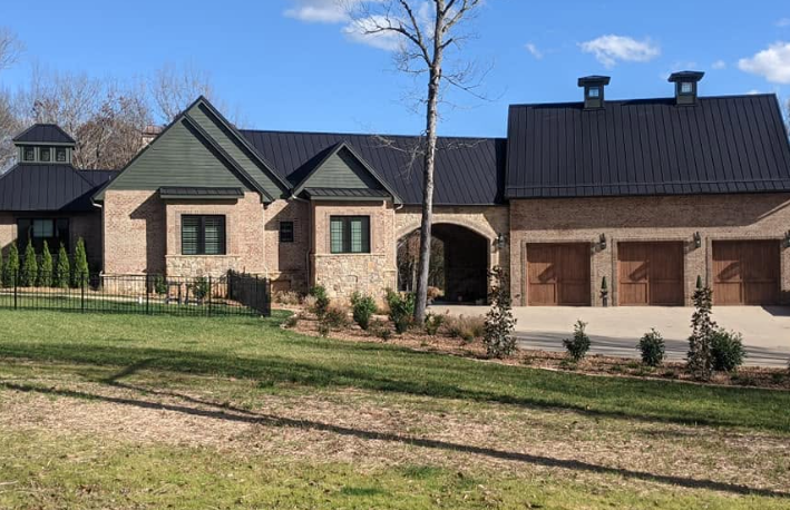 Stone house with dark roofs, a garage, and a grassy yard under a blue sky.