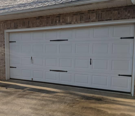 White double garage door on a brick house with black handles and decorative panels