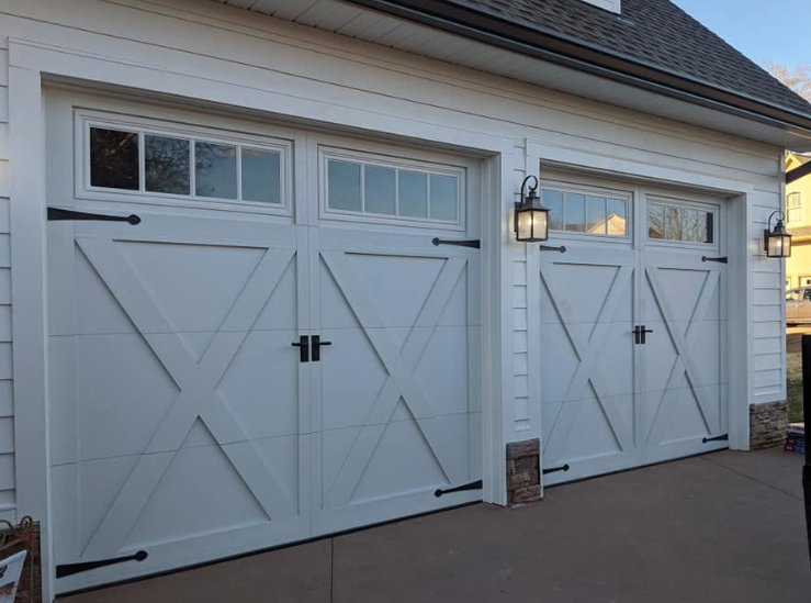 Two white garage doors with black hardware on a house exterior at dusk