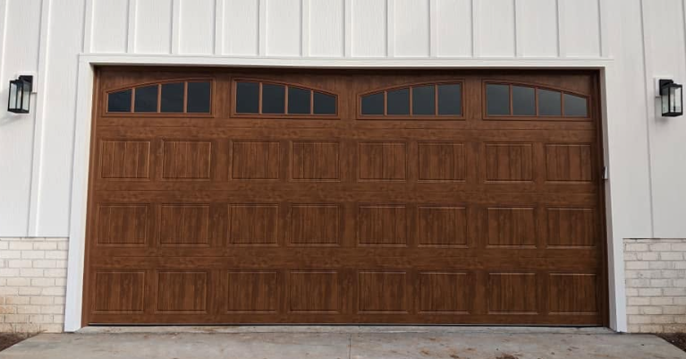 Closed brown wooden garage door on a white house exterior