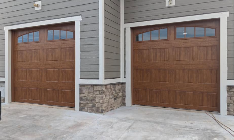 Two brown garage doors on a gray house with stone trim, viewed from the driveway