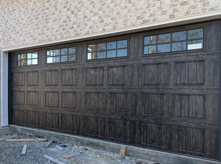 Dark wood-paneled garage door with small windows above, set in a stone exterior wall.