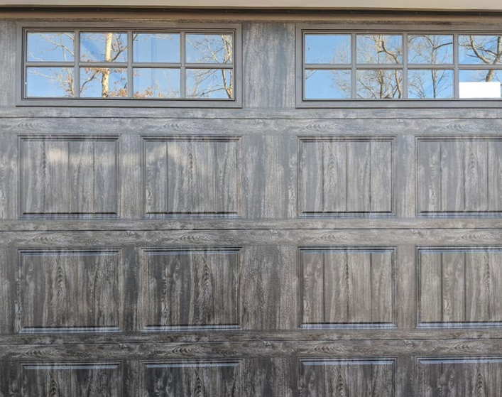 Weathered gray garage door with four upper windows reflecting bare tree branches
