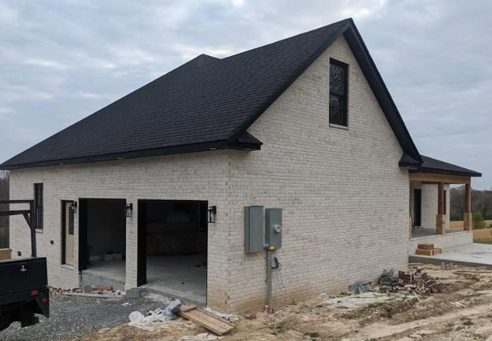 New house under construction with white brick walls, black roof, and open garage doors