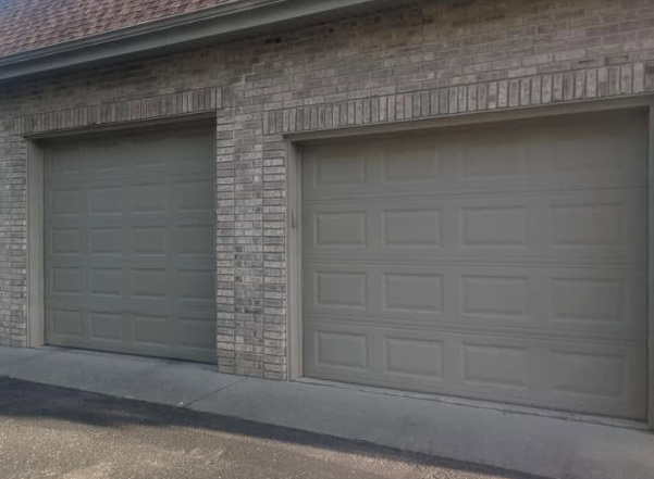 Two gray garage doors set in a brick building above a sloped driveway