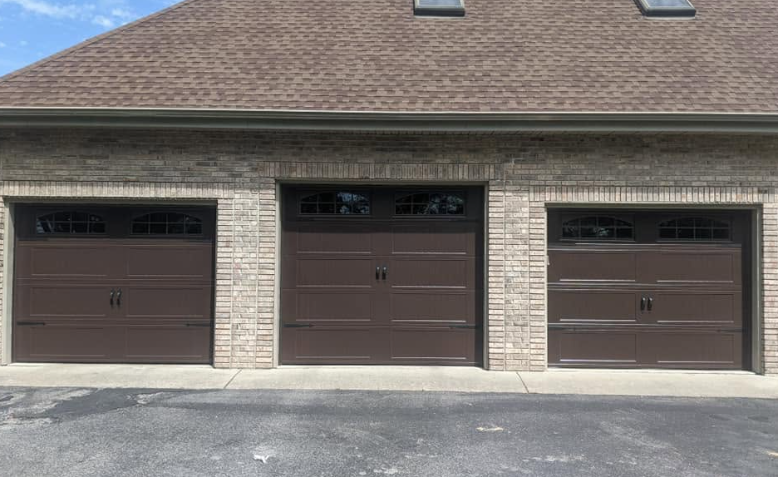 Three closed brown garage doors on a beige house with a shingled roof and asphalt driveway