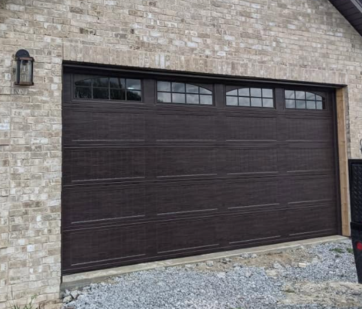 Dark brown garage door set in a beige brick wall beside a black wall lantern.