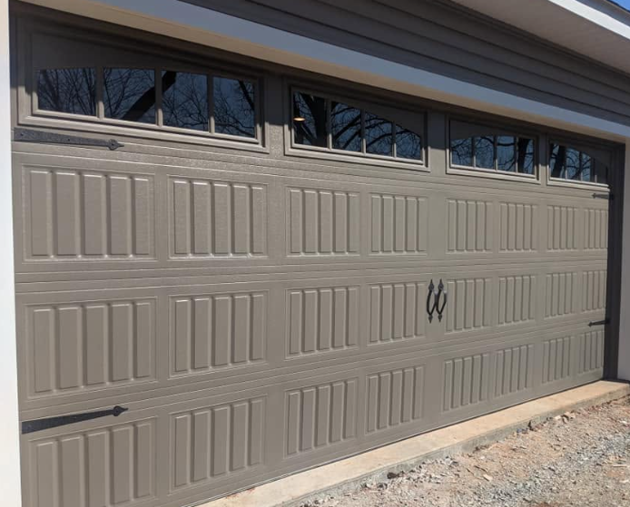 Tan double garage door with small windows along the top, seen on a house exterior.